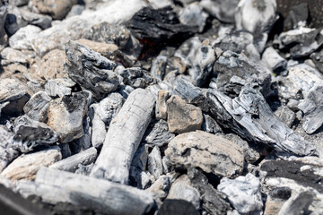 Charcoal pieces and ashes in a grill, showcasing the textures and contrasts typical of burnt wood and embers, illustrating a post-barbecue scene.