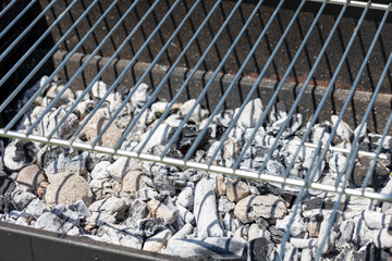 Charcoal pieces and ashes in a grill, showcasing the textures and contrasts typical of burnt wood and embers, illustrating a post-barbecue scene.