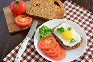 a toast with fried egg on a plate decorated with tomato slices