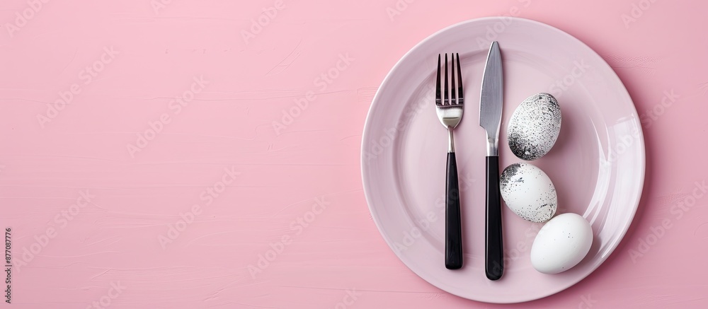 Poster top view of easter dinner setting featuring black and white eggs, knife, and fork on a pastel pink b