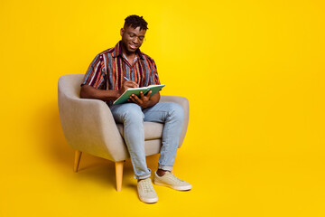 Full body portrait of nice young man sit chair write notebook wear shirt isolated on yellow color background