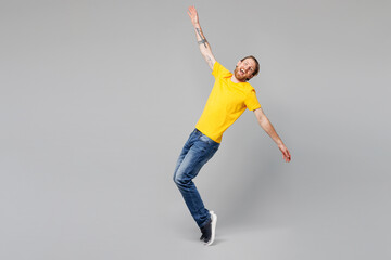 Fototapeta premium Full body young happy cheerful fun man he wear yellow t-shirt casual clothes stand on toes with outstretched hands lean back dance isolated on plain grey background studio portrait. Lifestyle concept.