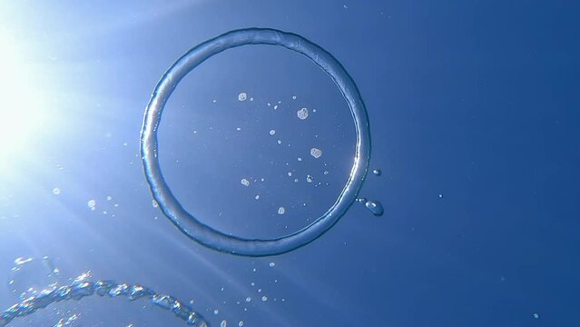 Air bubble ring under water. The freediver releases oxygen into the surface of the water in the shape of a ring. Beautiful water background with sun glare and air bubbles. Ring Bubble.