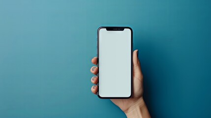 In a blue studio background a hand holds a phone with a blank screen promoting an app The mockup offers a wide view and copy space