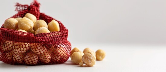 Macadamia nuts are presented in a red mesh bag set against a white backdrop with copy space image.