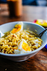 Boiled noodles with pieces of egg isolated in a white bowl on a wooden table.