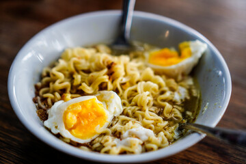 Boiled noodles with pieces of egg isolated in a white bowl on a wooden table.