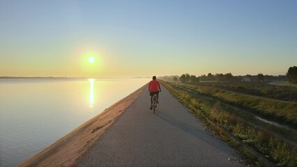 Man riding bike on riverside cycle path at sunset. Aerial drone follow shot