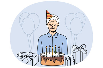 Sad old birthday person celebrating alone standing near table with gifts and cake and needing support of friends. Frustrated grandfather is sad because there are no guests for birthday parties