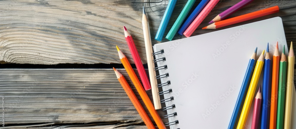 Aufkleber Wooden table with an empty notebook and colorful pencils, providing copy space image.