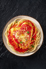 Chicken Parmesan, Italian pasta dish. Breaded chicken breast with cheese and spaghetti with tomato sauce, shot from the top on a black slate background