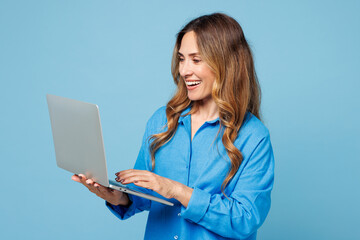 Side view smart young IT woman wear shirt casual clothes hold use work on laptop pc computer browsing internet isolated on plain pastel light blue cyan background studio portrait. Lifestyle concept.