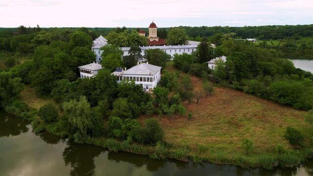High angle drone footage of Manastirea Caldarusani and it's surrounding lake on a warm summer day. Calm water around a forrest in which a monastery is situated. Aerial shot christian of temple.
