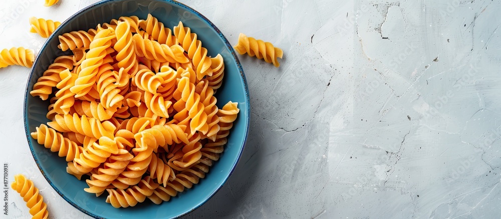 Poster ample copy space surrounds a vibrant array of spiral pasta in a blue bowl placed on a white surface.