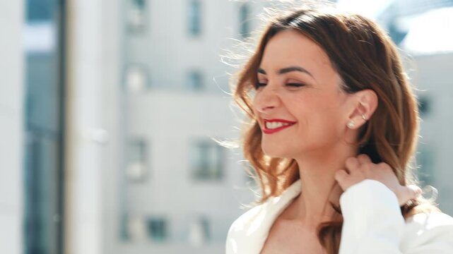 Young beautiful brunette woman wearing nice trendy white suit jacket. Sexy smiling model posing in the street at sunny day. Fashionable female outdoors. Cheerful and happy. Evening makeup, red lips