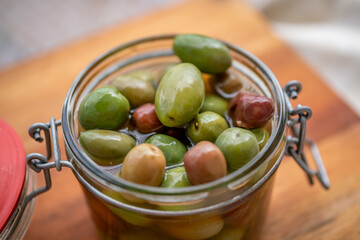 Olives in brine in the glass jar with open cover on wooden cutting board