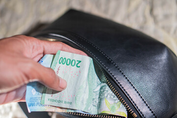 Hand placing Indonesian rupiah into black leather bag