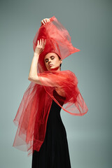 A young, beautiful ballerina in a black dress and red shawl, dancing gracefully.