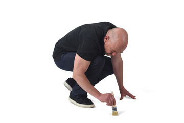 profile view of a man crouching painting on the floor with a brush on white background