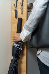 A woman in office attire picks up an umbrella next to the wooden cabinet before she goes outside, a...