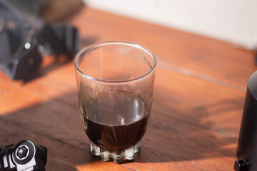 Half-full glass of black coffee on wooden table