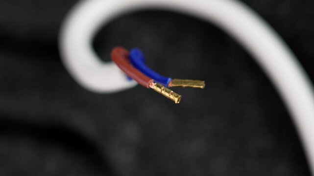 Electrical wires with exposed copper terminals of Insulated white cable in the hand of an electrician wearing black protective gloves closeup