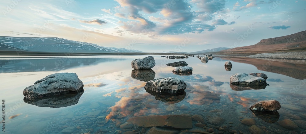 Poster Tranquil nature scene with rocks in the foreground mirrored in a lake under a twilight sky providing a serene ambience for a copy space image