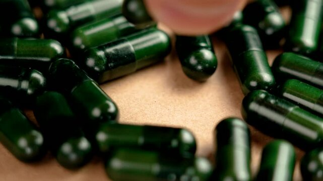 Hand of a sick patient taking a green herbal pill from a pile of medicines. Macro shot. Bioavailability concept