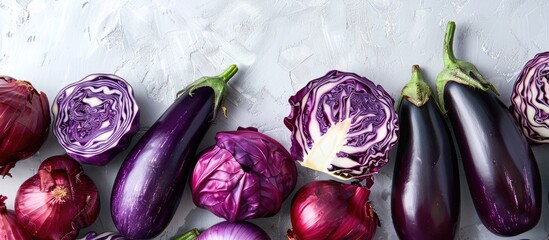 Diverse selection of fresh purple vegetables like eggplants and red cabbage arranged against a plain background ideal for copy space image