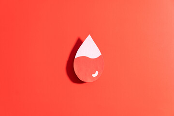 Blood drop with low blood level made from paper on red background. Concept of hematologic disorders...