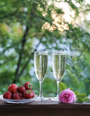 Glasses of champagne and strawberries on a terrace in a summer garden against the backdrop of evening sunlight
