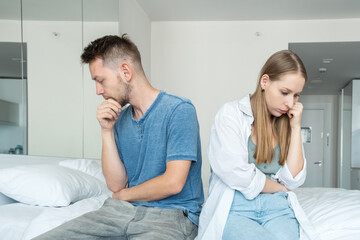Fototapeta premium Unhappy couple in argument with disappointed woman and sad man sitting with their backs to each other after conflict and quarrel. Upset girl thinking of relationship problems with boyfriend