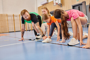Diverse group of young people energetically stand together on top of a vibrant blue floor in a lively classroom, under the guidance of a male teacher.