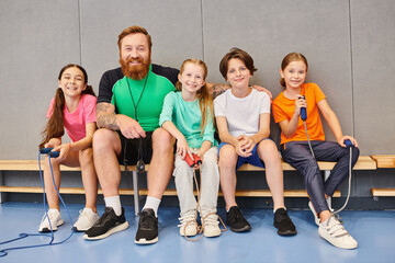 Fototapeta premium A man with a beard, a teacher, sitting on a bench surrounded by happy, diverse children of various ages, engaging in conversation and learning together.