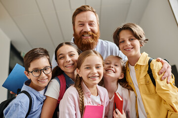 A diverse group of children stand next to a man in a bright classroom setting