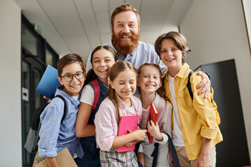 Obraz premium A man teacher engages with a diverse group of children in a lively hallway, imparting knowledge and guidance in a bright educational environment.
