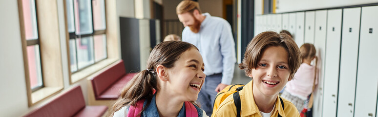 A pair of kids standing side by side, sharing a tender moment together in a bright, lively classroom setting.