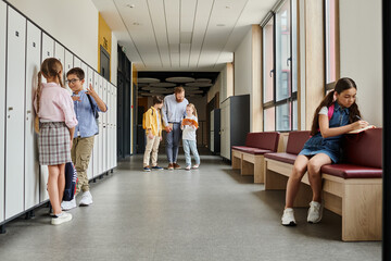 group of children stand in hallway beside lockers while a teacher instructs them in a bright, lively classroom setting.