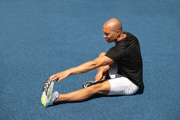 Athlete stretching legs after workout or run in public park. Outdoors training. Morning routine. Summer workout .