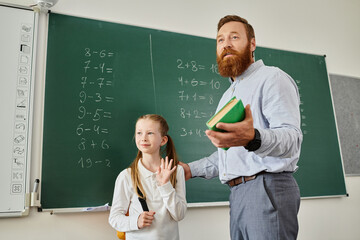 A man in casual clothing stands beside a little girl, both looking attentively at a blackboard full...