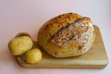 classic sourdough artisan bread with added potatoes on a wooden board on a pastel pink background. Potato bread.