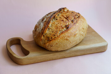 classic sourdough artisan bread with the addition of dried onions and onions on a wooden board on a pastel pink background.