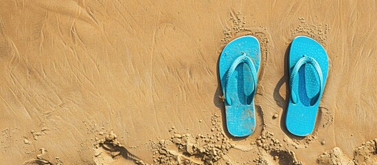 Overhead view of blue flip flops on a sandy beach with a designated copy space image