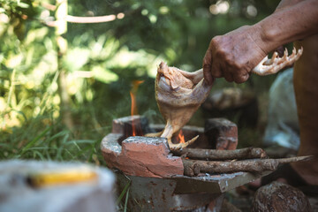 Hand holding raw chicken over an Asian fire stove for cooking.