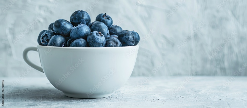 Poster side view of a white ceramic cup filled with fresh washed blueberries on a light grey backdrop offer