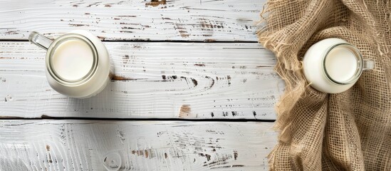 An overhead shot of a glass bottle and cup filled with milk on a white wooden table with a burlap tablecloth providing copy space image