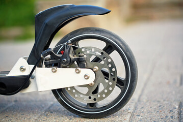 Scooter wheel mechanic disc brake system with ventilated brake disk and brake caliper on rear wheel closeup. Rear wheel of scooter with disc brakes. Wheel scooter back view