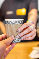 Close-up of hands exchanging a patterned takeaway coffee cup, highlighting human interaction and daily life