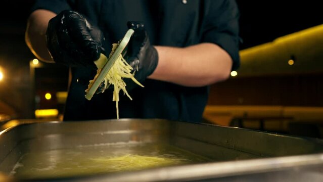 close up in a restaurant in a rib bar in the central hall chef in black gloves pours grated potatoes into an iron container