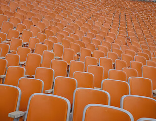 Fototapeta premium Rows of empty orange stadium seats. Ideal for sports, events, or concepts of isolation and anticipation.